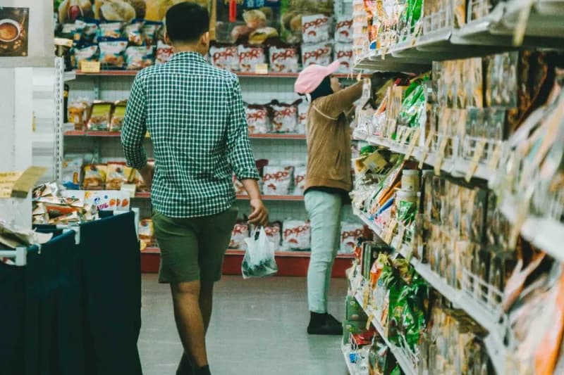 Shoppers in a grocery store aisle with packaged snacks on shelves